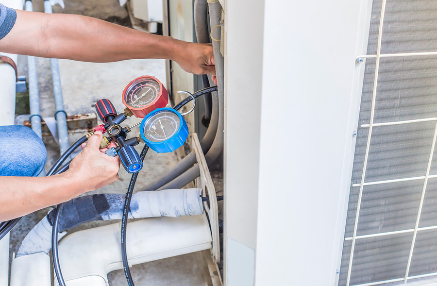 Air repair mechanic using measuring equipment for filling industrial factory air conditioners
