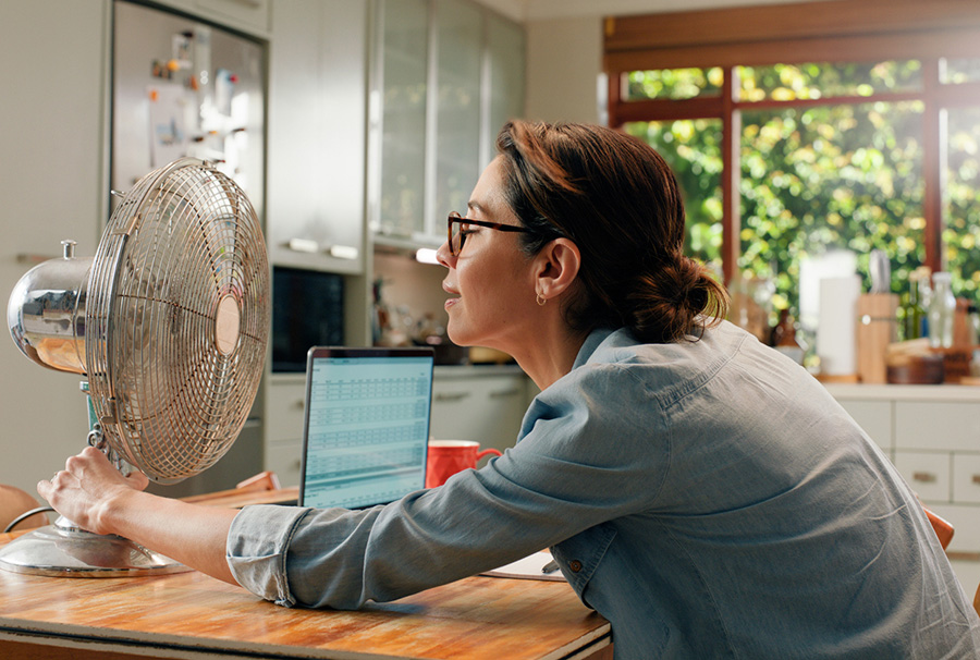 Woman, fan and laptop in home with heat wave as freelance copywriting for remote work, email or kitchen