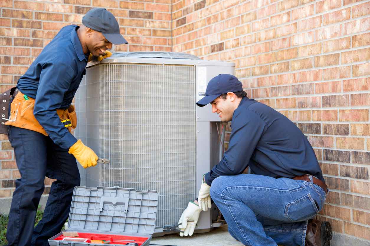 Two HVAC technicians in blue work shirts are installing a new outdoor unit